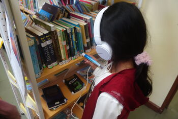 Kind mit Kopfhörern und Stift am Bücherregal