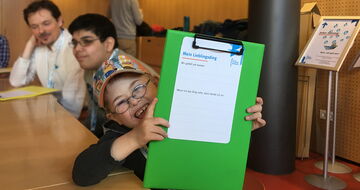 Junge mit Downsyndrom hält fröhlich einen Fragebogen in die Kamera