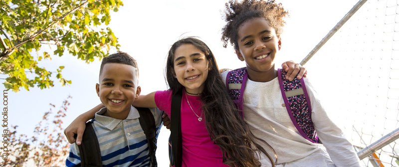 Schulbezogene Sozialarbeit an der Mercator-Grundschule; Berlin Steglitz-Zehlendorf, im Ortsteil Lichterfelde, drei fröhliche Kinder Arm in Arm